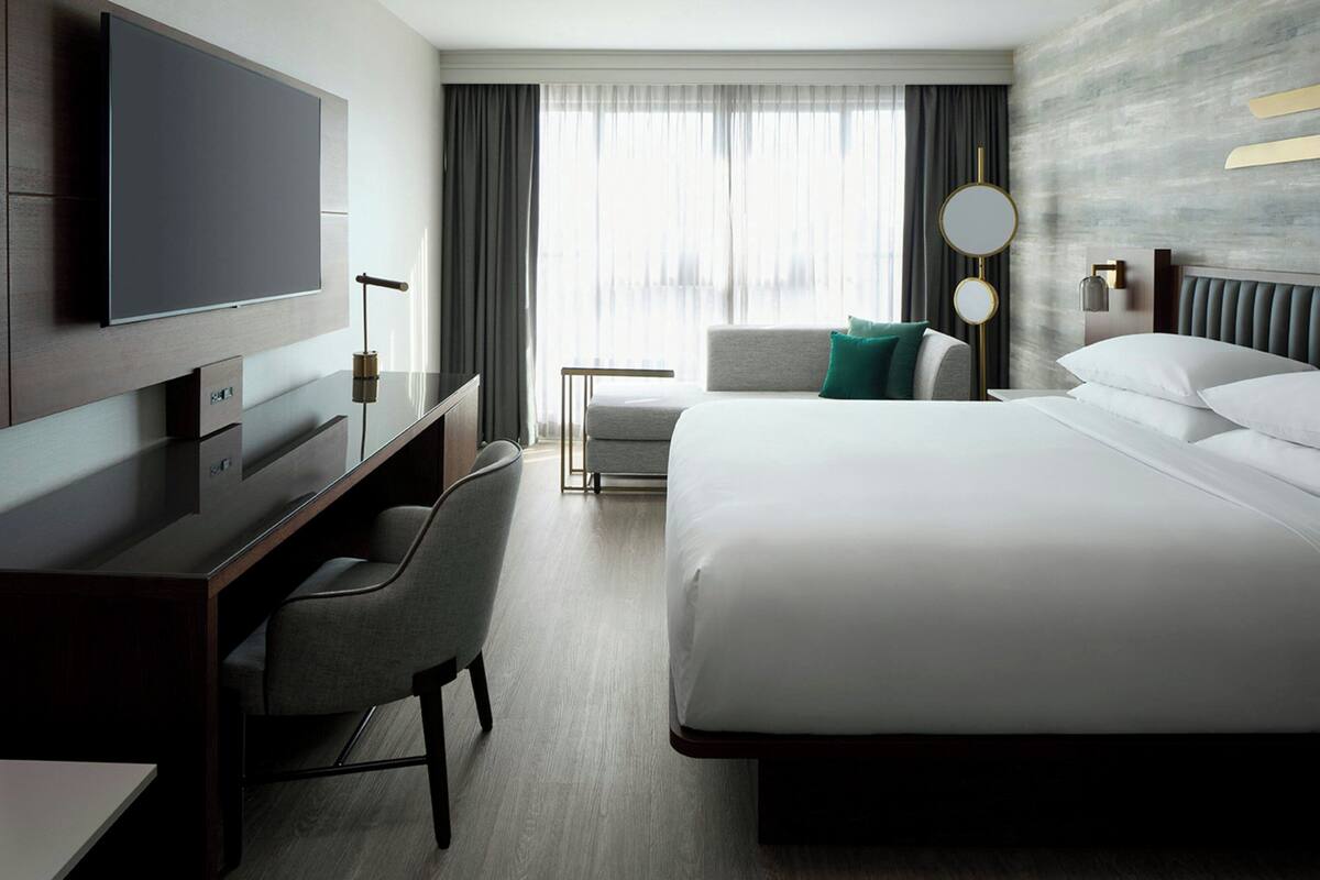 A hotel room with a large bed, a desk with a chair, a television, and a window with curtains.