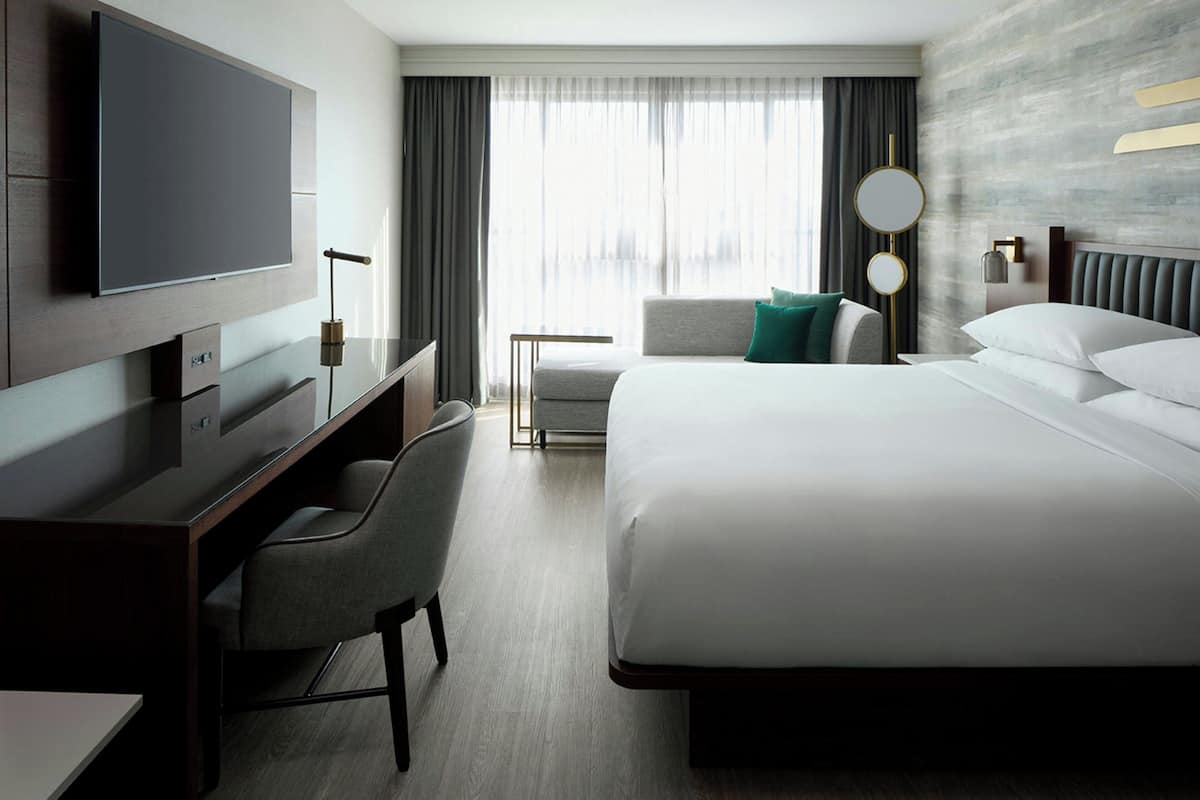 Una habitación de hotel con una cama grande, un escritorio con silla, televisión y ventana con cortinas.