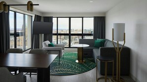 Una habitación de hotel moderna con un ventanal grande, una mesa redonda, un sofá y un televisor.