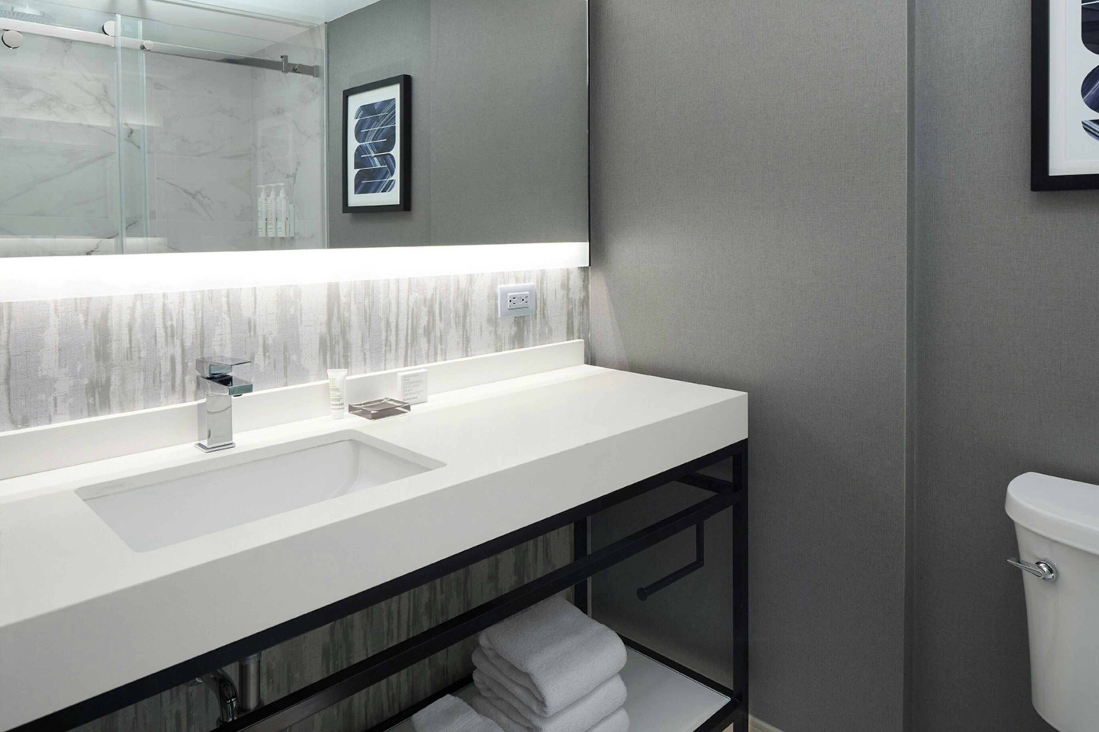 Un baño moderno con un espejo grande, un lavamanos blanco y una cabina de ducha de vidrio.