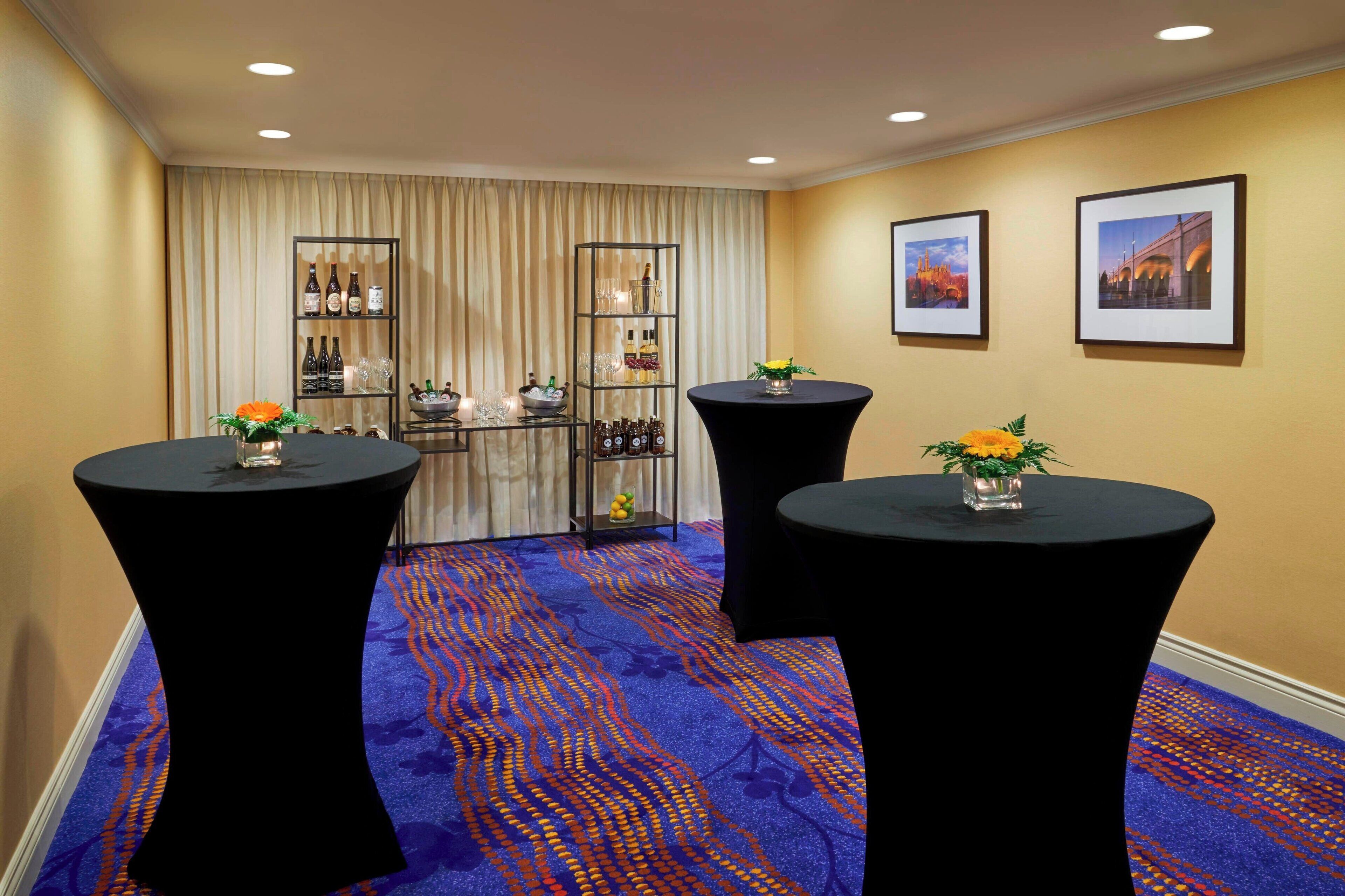 A hotel lobby with two round tables, a bar area with shelves of bottles, and framed pictures on the wall.