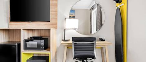 Quarto de hotel com televisão de tela plana, micro-ondas, cofre, escrivaninha com cadeira, espelho e tábua de passar roupa amarela.
