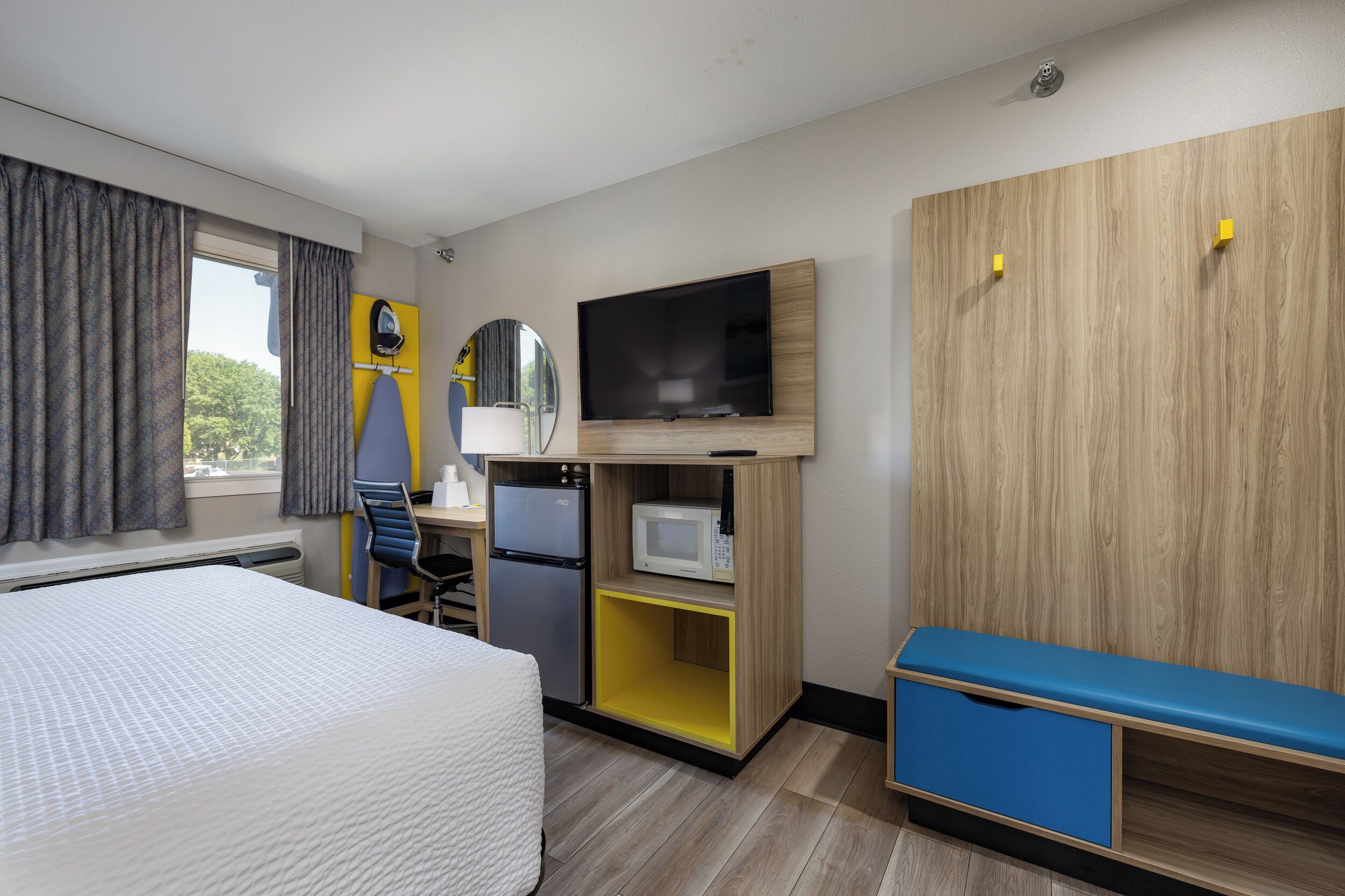 A hotel room with a bed, a desk with a computer, a microwave, a TV, and a wardrobe.