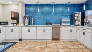 A modern kitchen with white cabinets, a blue brick backsplash, and various appliances including a coffee maker and microwave.