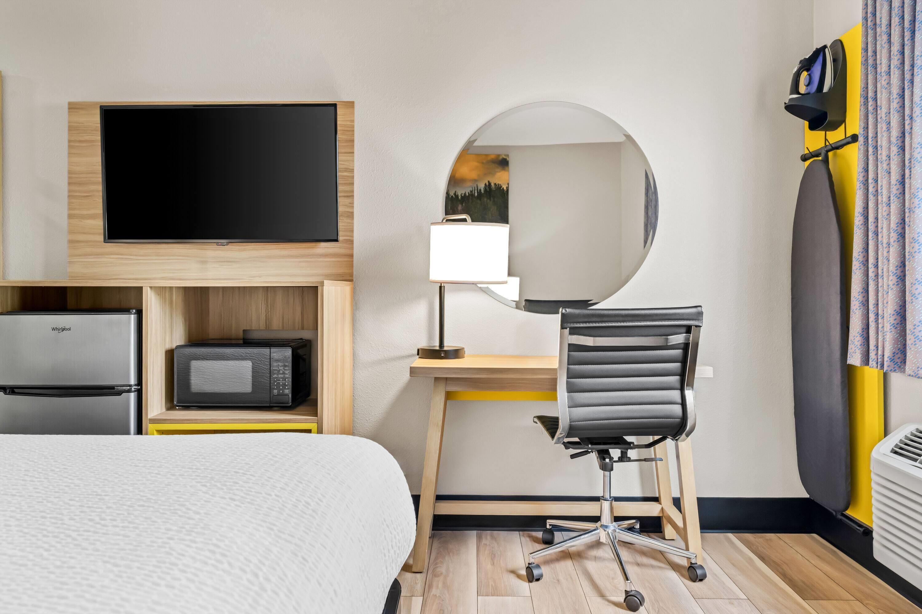 A hotel room with a bed, a desk with a chair, a flat-screen TV, a microwave, and a refrigerator.