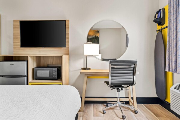 A hotel room with a bed, a desk with a chair, a flat-screen TV, a microwave, and a refrigerator.