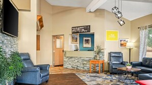 A hotel lobby with leather chairs, a reception desk, a potted plant, and a wall-mounted sign.