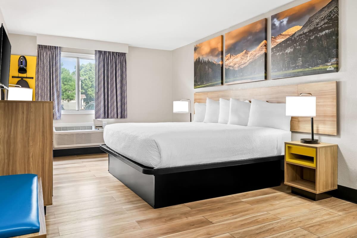 A modern hotel room with a large bed, bedside tables, a desk, and a window with curtains.