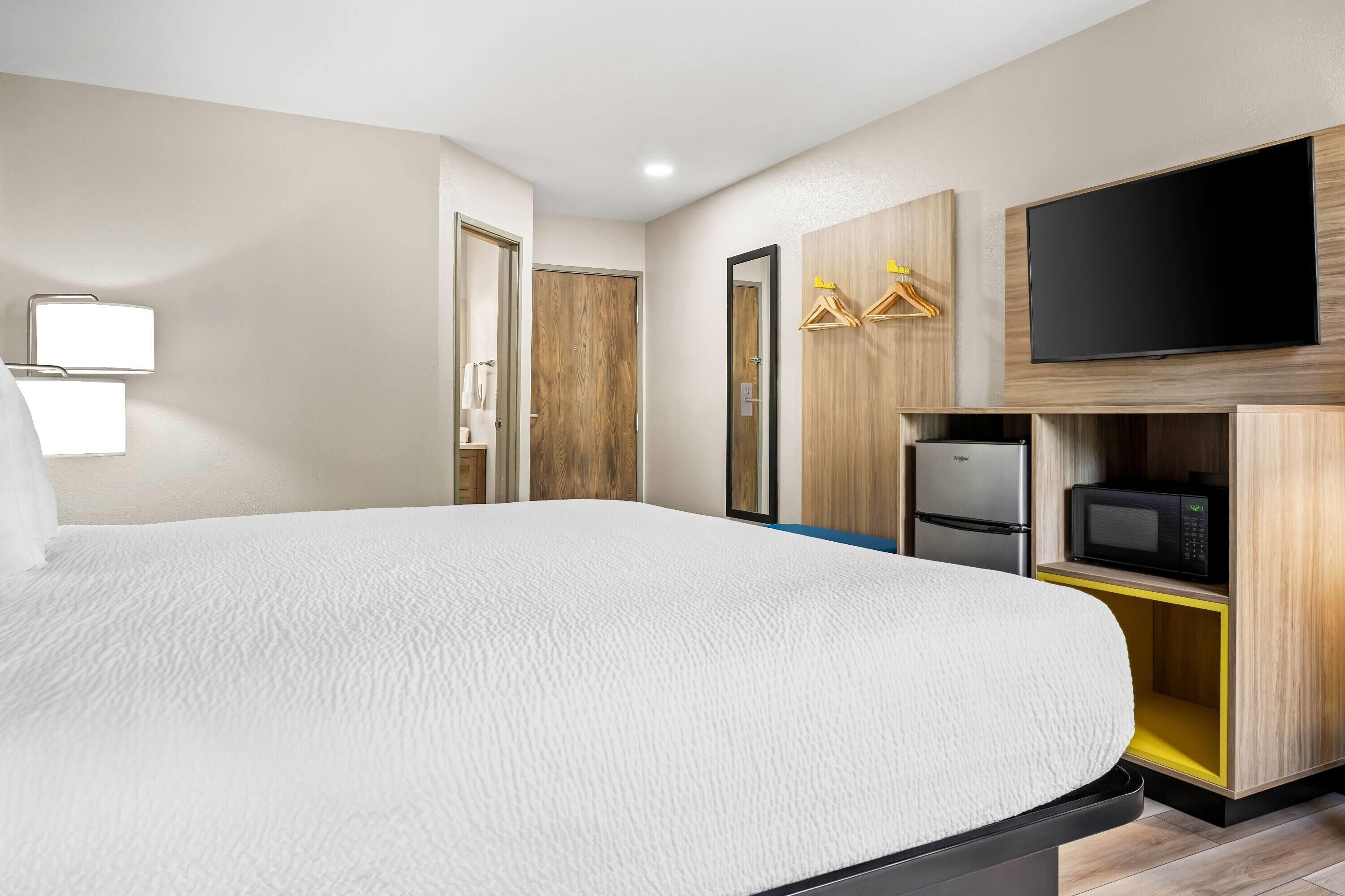 Ein Hotelzimmer mit einem großen Bett, einem Flachbildfernseher, einer Mikrowelle und Holzschränken.