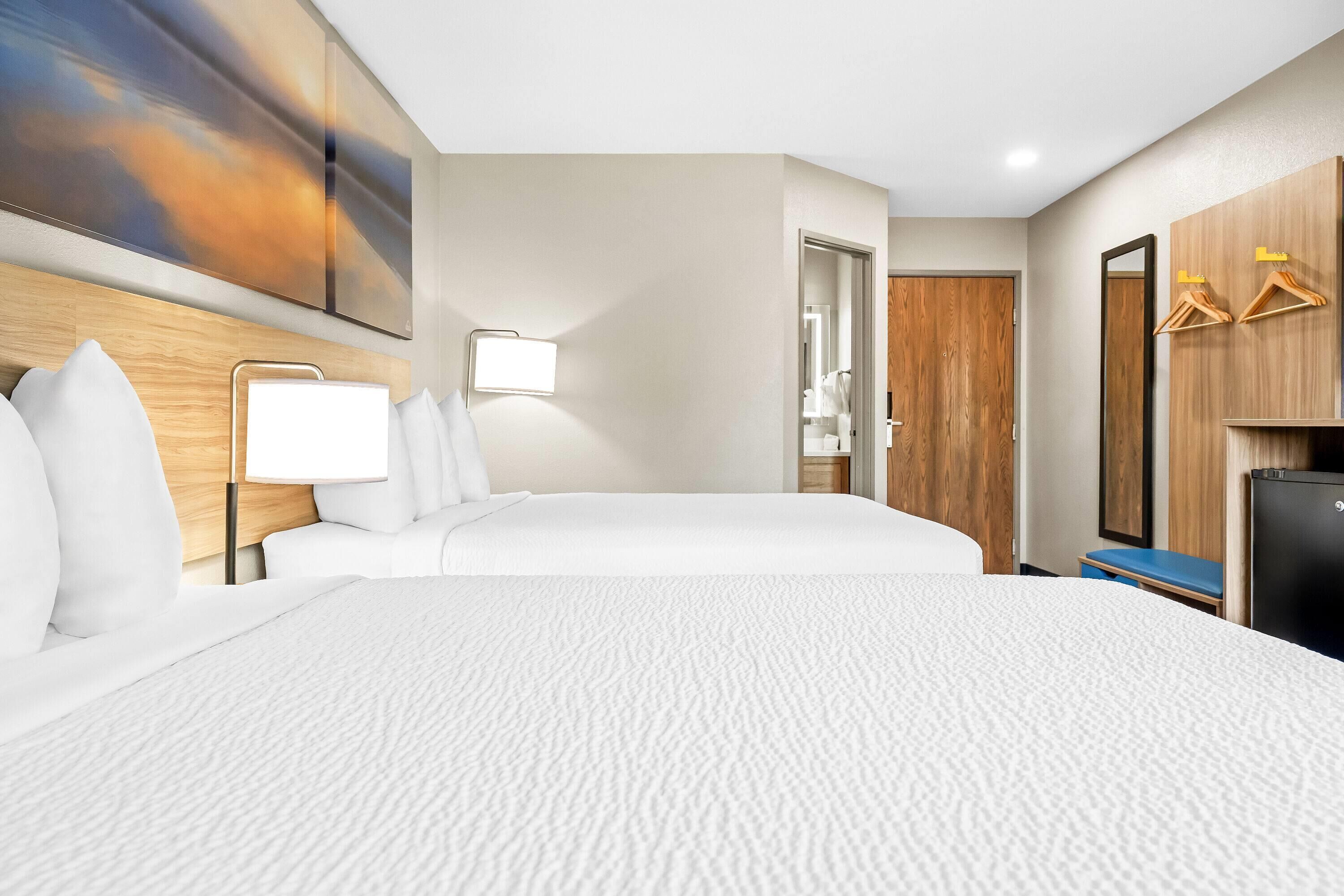 A hotel room with a large bed, a bedside table with a lamp, a wooden headboard, a wardrobe with wooden doors, and a mirror.