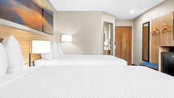 Una habitación de hotel con una cama grande, una mesita de noche con lámpara, un cabecero de madera, un armario con puertas de madera y un espejo.