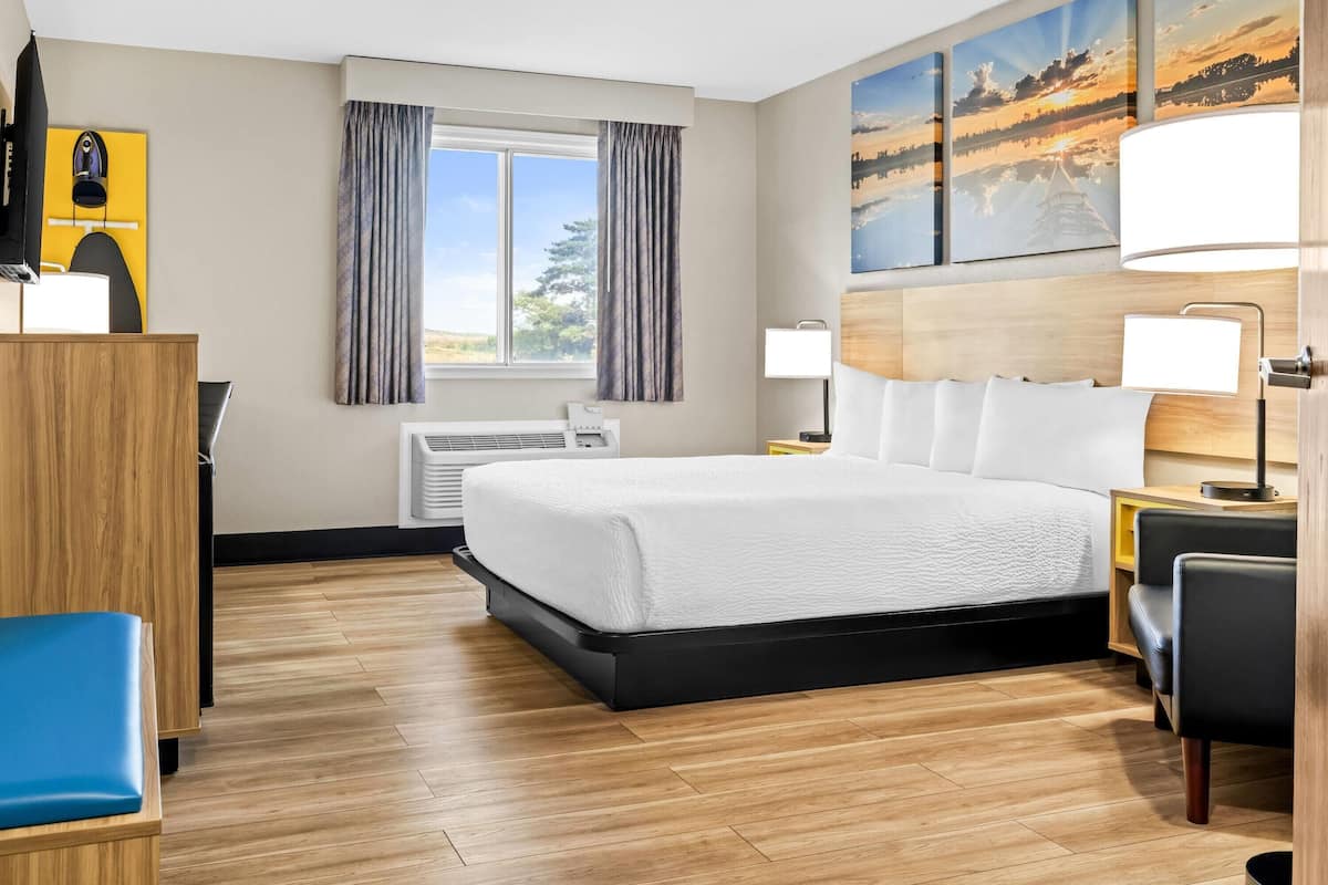 A hotel room with a large bed, a desk, a chair, a window with curtains, and artwork on the wall.