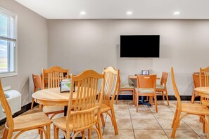 Un salón de conferencias con mesas y sillas de madera, un televisor de pantalla plana en la pared y un ventanal con persianas.