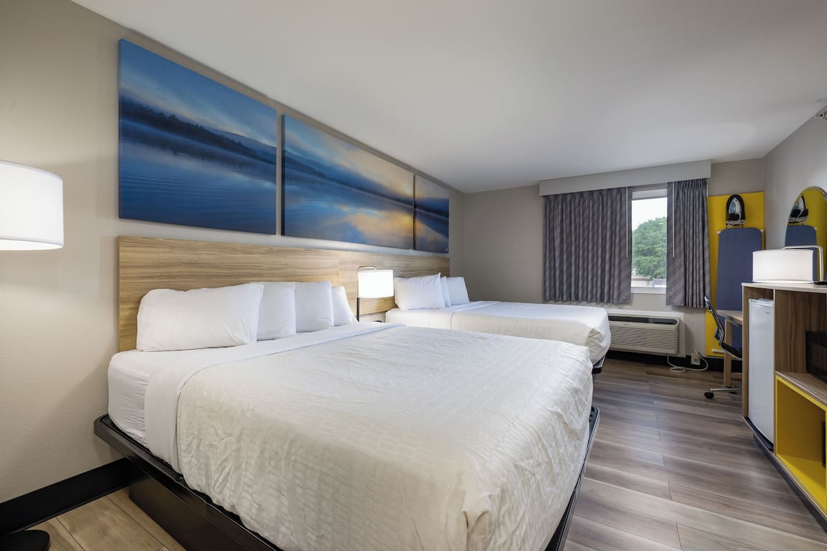 A hotel room with two beds, a large painting above the beds, a desk with a computer, and a window with curtains.