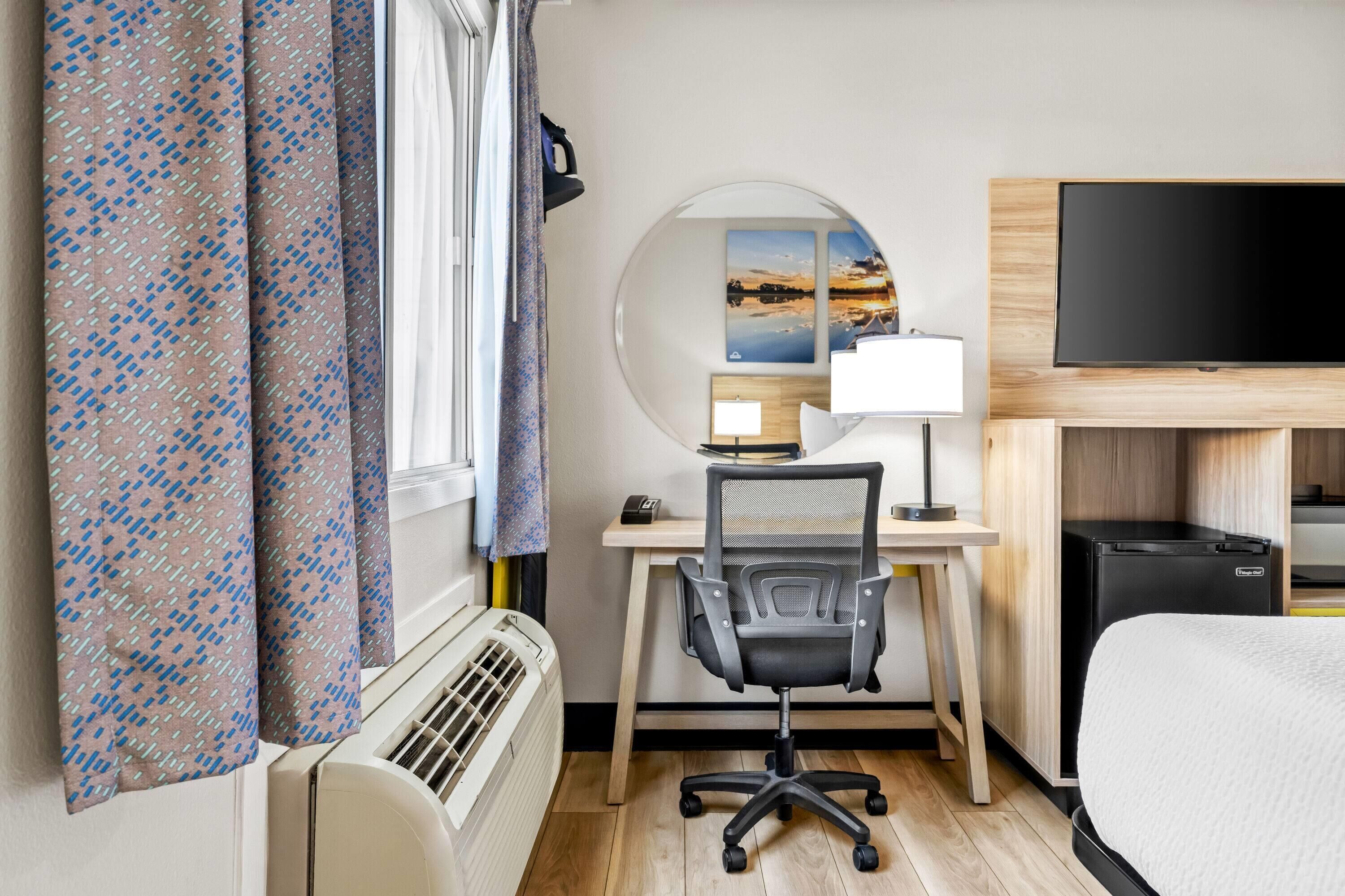 Habitació d'hotel amb llit, escriptori amb cadira, televisió de pantalla plana, un calefactor i cortines.