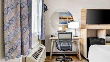 Habitació d'hotel amb llit, escriptori amb cadira, televisió de pantalla plana, un calefactor i cortines.