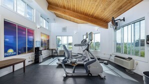 A gym with exercise equipment, large windows, and a wooden ceiling.