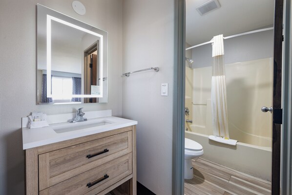 A modern bathroom with a white sink, wooden vanity, a large mirror, and a glass-enclosed shower area. - Days Inn by Wyndham Billings (Billings)