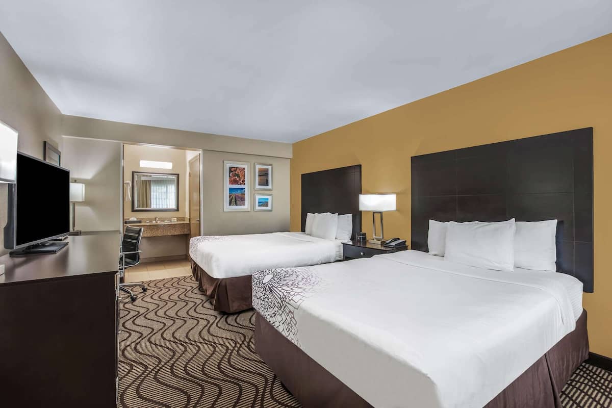 A hotel room with two beds, a desk, a TV, a bathroom, and a mirror.