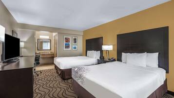 A hotel room with two beds, a desk, a TV, a bathroom, and a mirror.