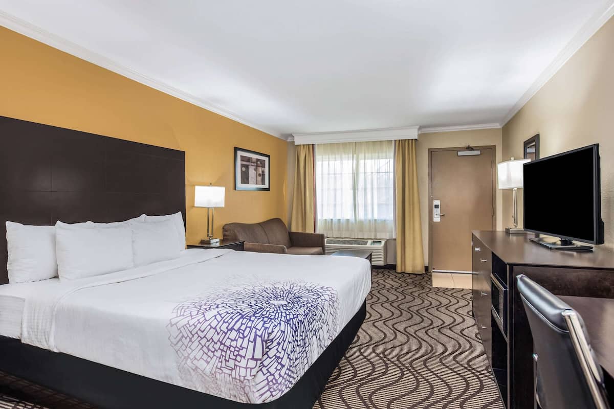 A hotel room with a large bed, a desk, a television, and a window with curtains.