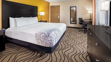 A hotel room with a large bed, a desk, a chair, a dresser, and a mirror.