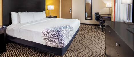 A hotel room with a large bed, a desk, a chair, a dresser, and a mirror.