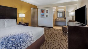 A hotel room with a large bed, a desk, a television, a bathroom with a sink and mirror, and a patterned carpet.