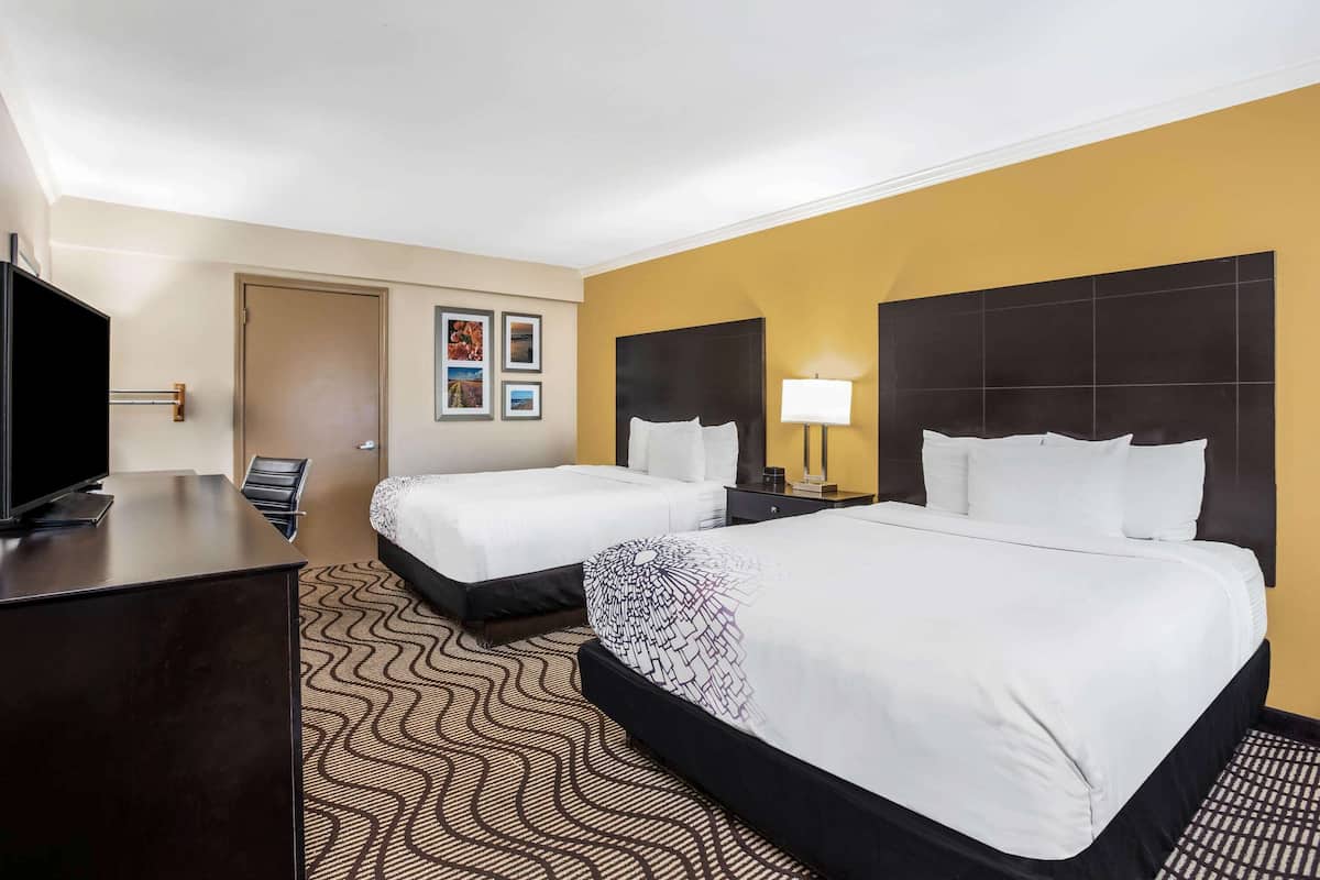 A hotel room with two beds, a desk, a TV, and a door.
