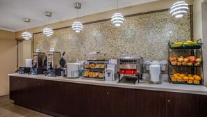 A breakfast bar with coffee machines, a waffle maker, and a fruit display.