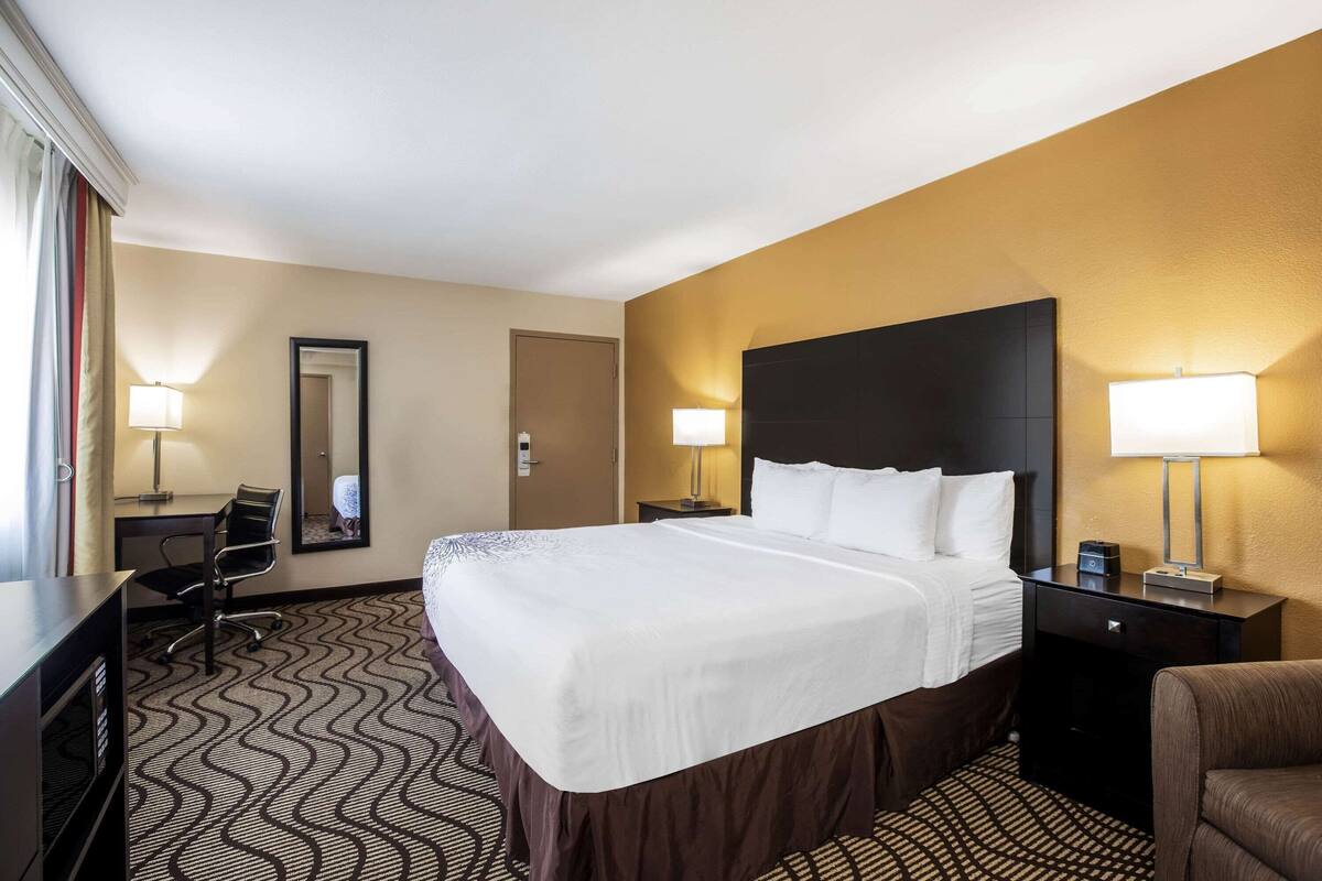 A hotel room with a large bed, a desk, a chair, and two bedside lamps.