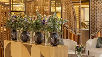 Een receptiegedeelte met een houten console, vazen met bloemen en een zithoek met een bank en fauteuils.