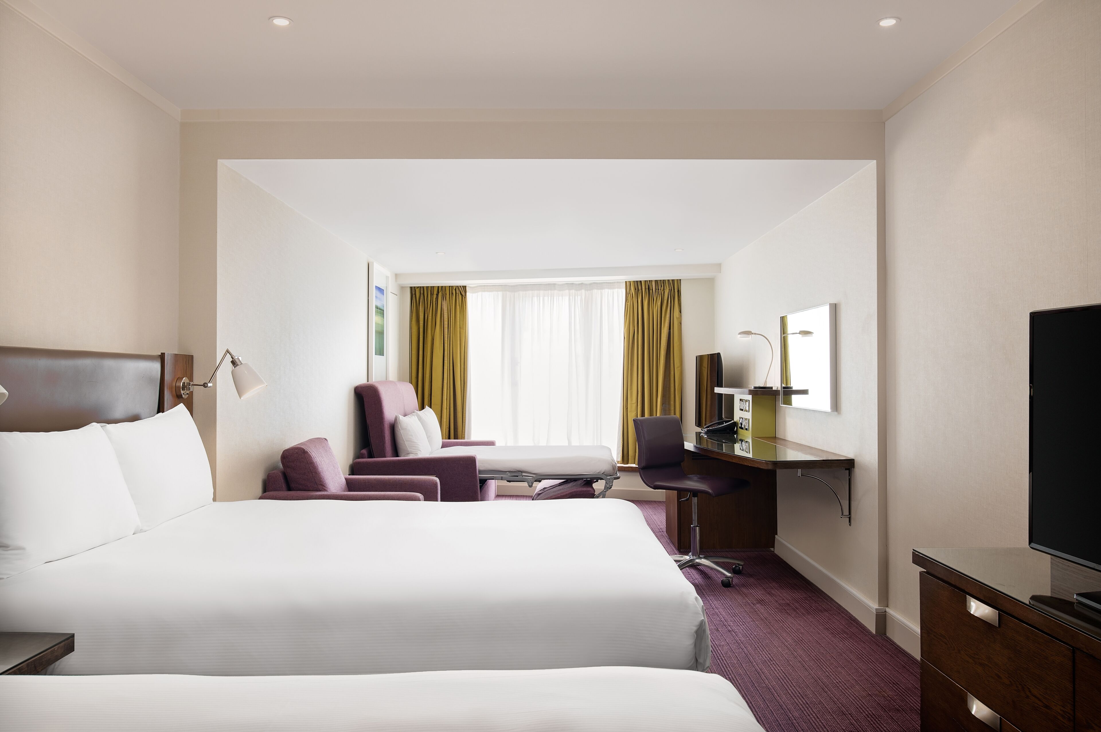 A hotel room with two beds, a desk, a chair, a TV, and a window with curtains.