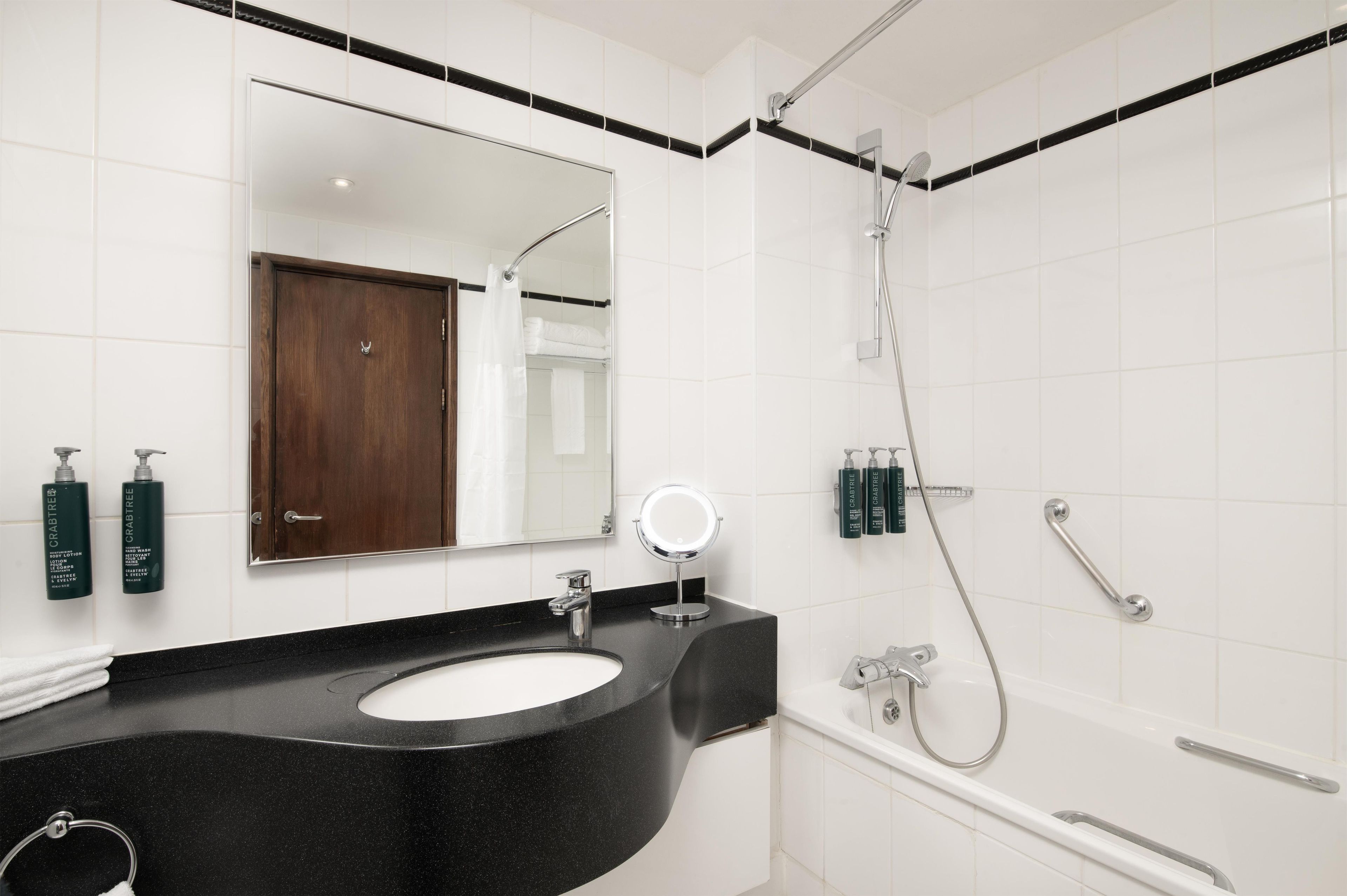 Ein modernes Badezimmer mit einem schwarzen Waschtisch, einem Spiegel und einer Dusche mit Duschbrause.