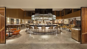 A modern bar area with a central bar, seating, and a polished floor. - Hilton London Metropole (London)