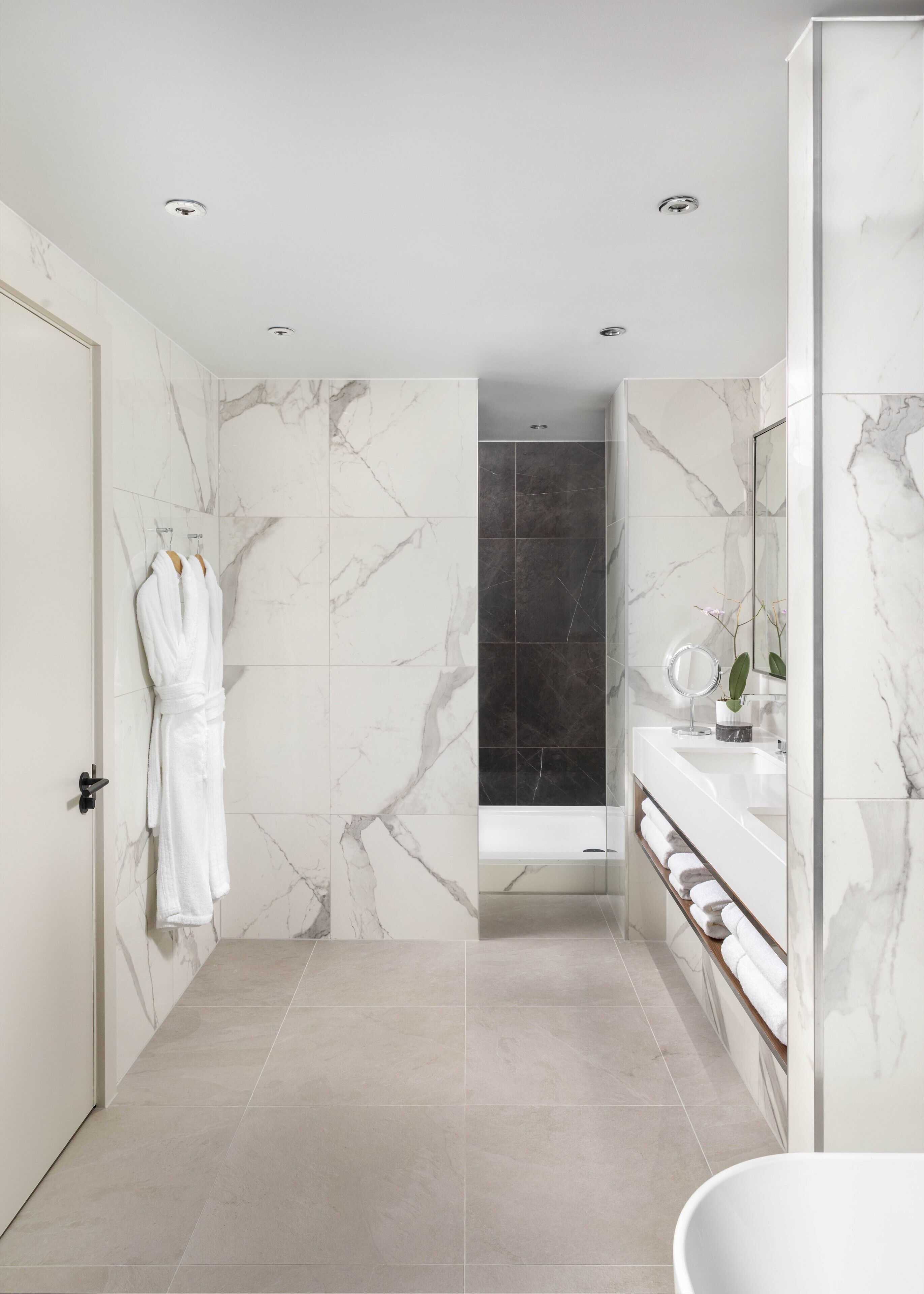 A modern bathroom with marble walls, a bathtub, and a vanity with a mirror.