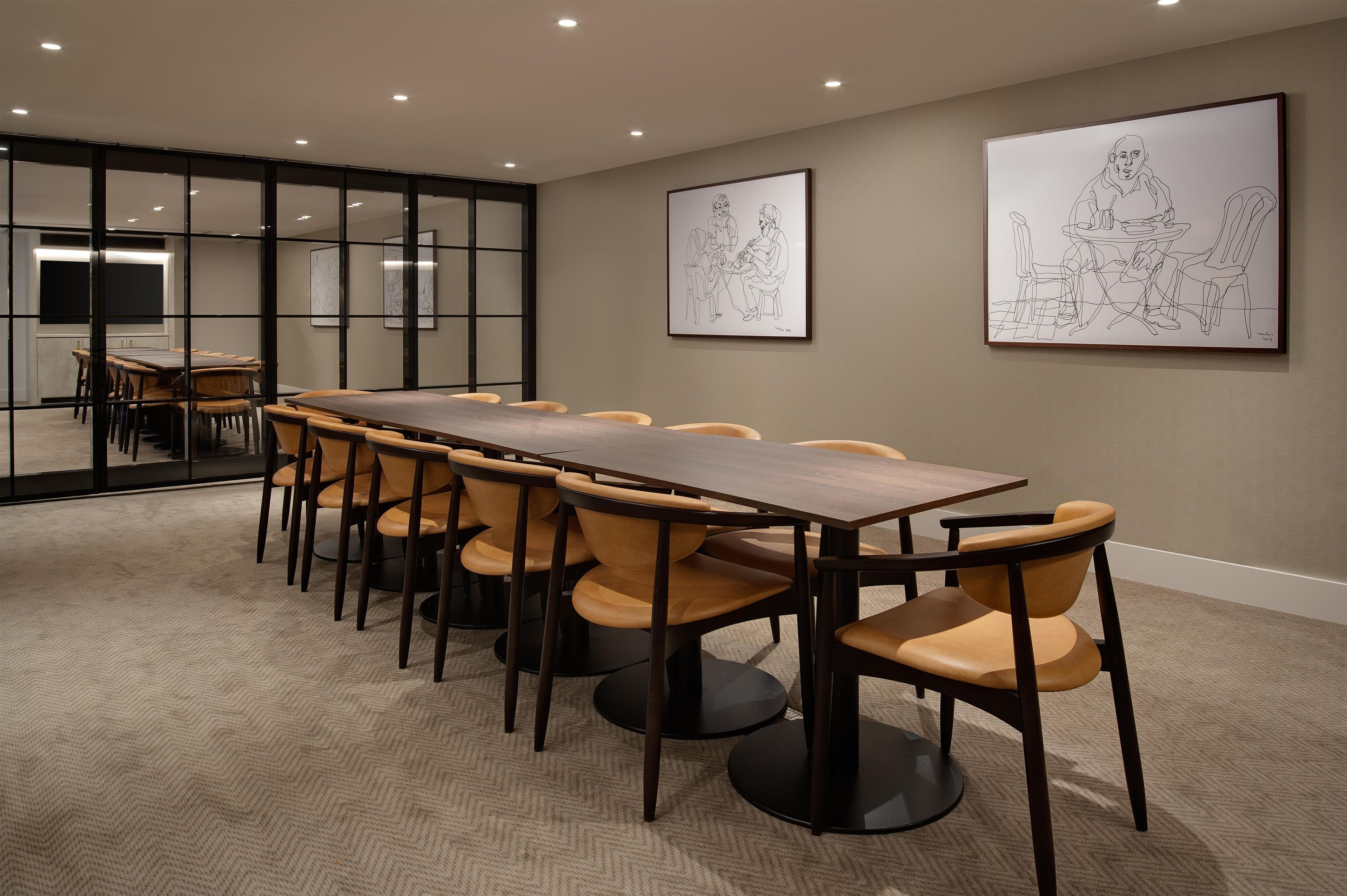 A conference room with a long table and chairs, glass walls, and artwork on the walls.