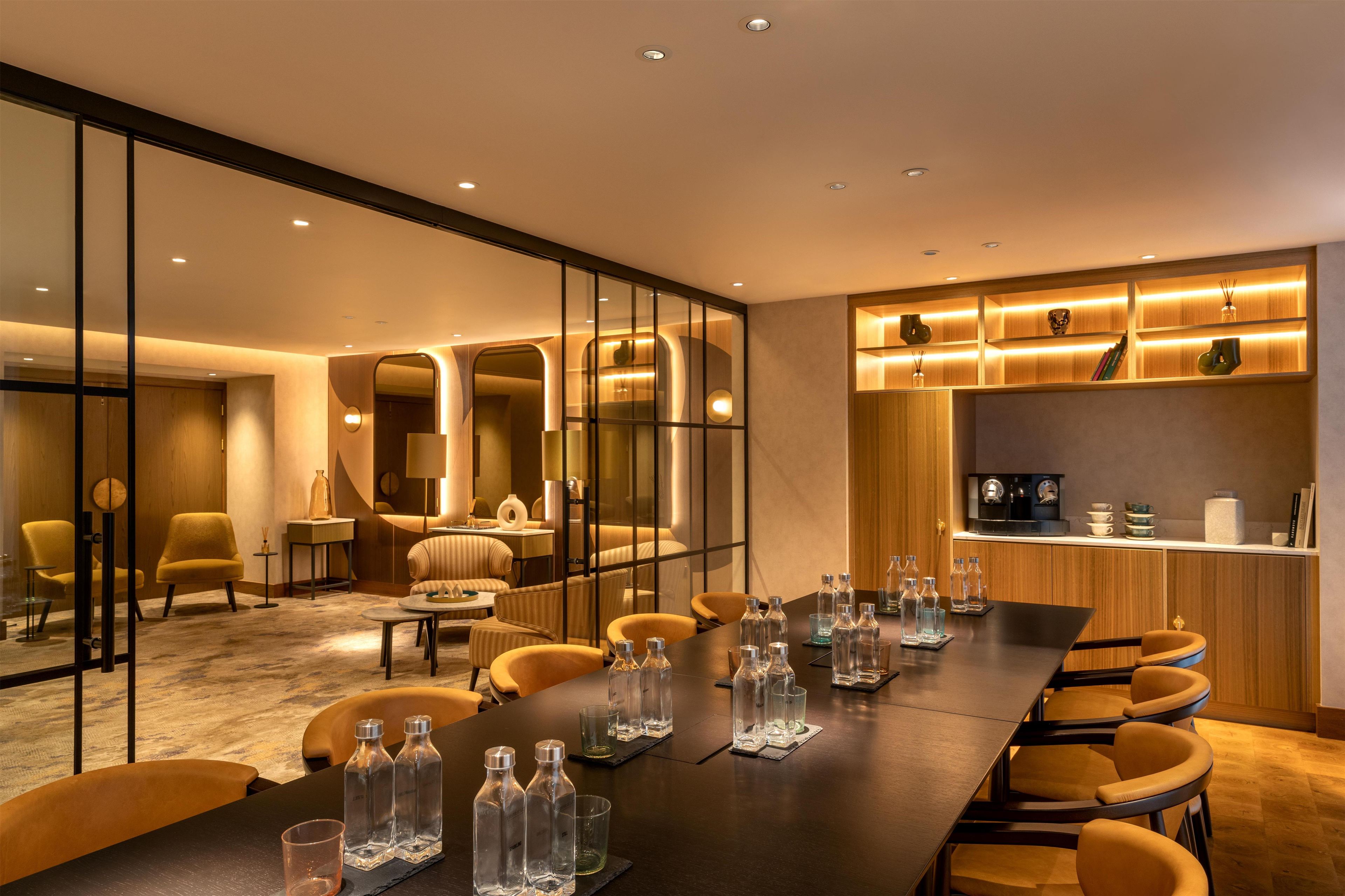 Una habitación de hotel moderna con una larga mesa de comedor, asientos cómodos y una zona de cocina.