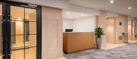 A modern reception area with a reception desk, a potted plant, and a glass door entrance.