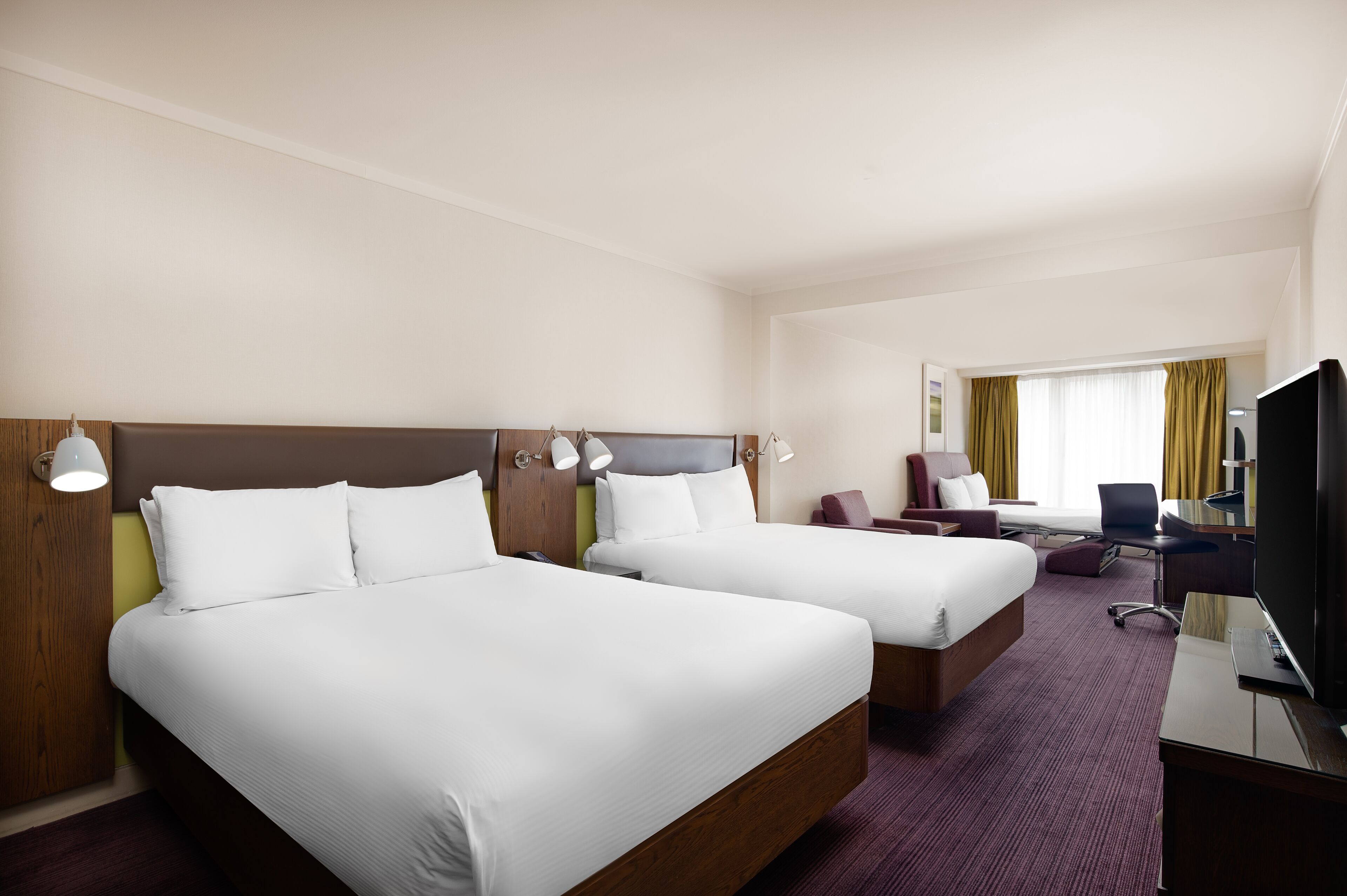 A hotel room with two beds, a desk, a chair, and a television.