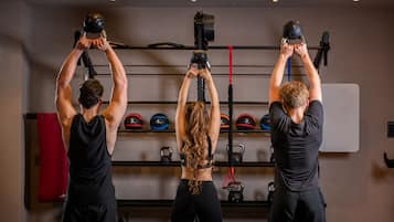 Tres personas haciendo ejercicio con bandas de resistencia en un gimnasio con pesas de cañón y un saco de boxeo.