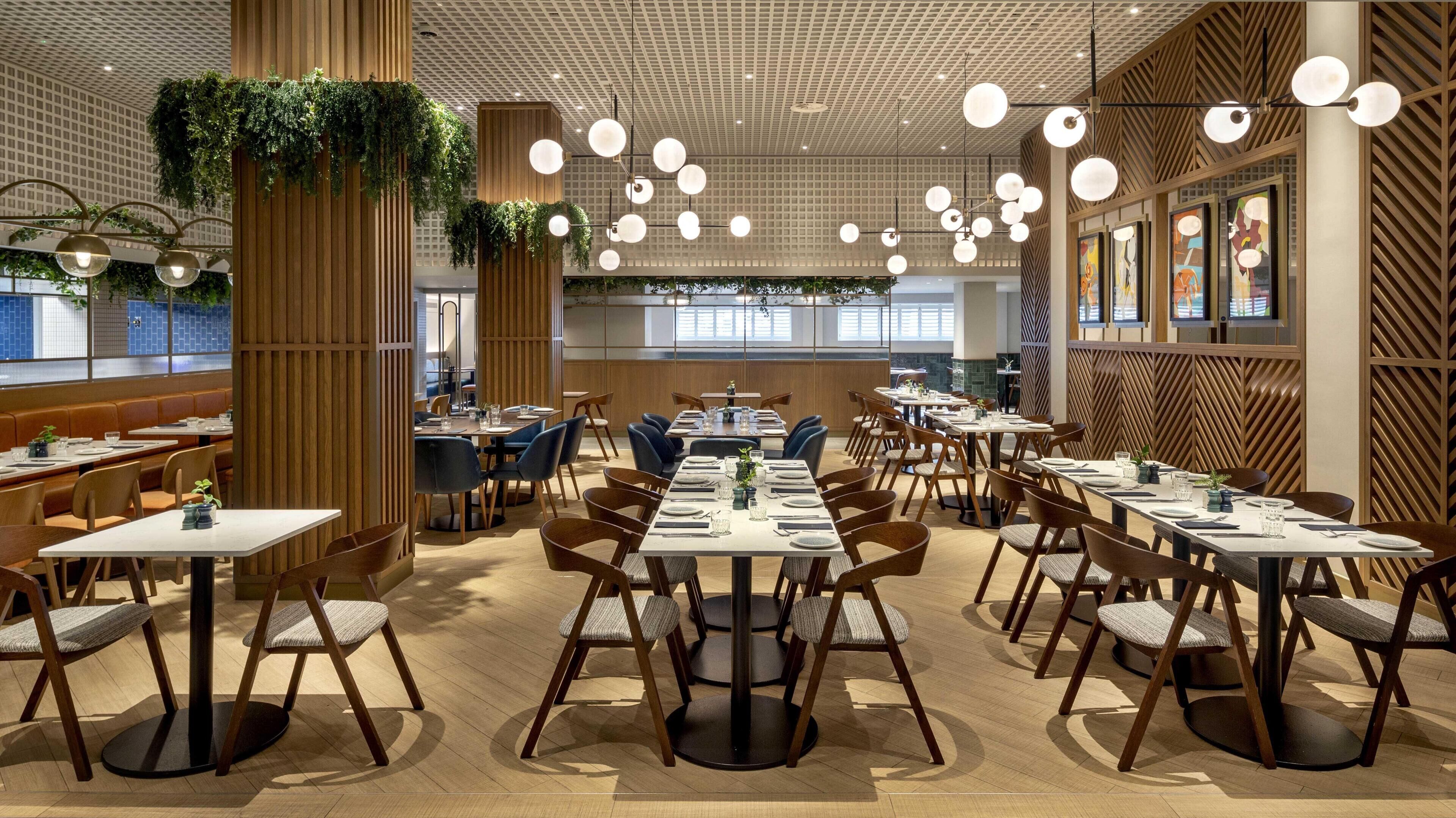 En moderne restaurant med lange fællesspisesteder, separate siddepladser og hængende planter.