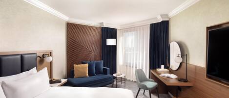 A hotel room with a large bed, a desk with a chair, a small table, and a TV.