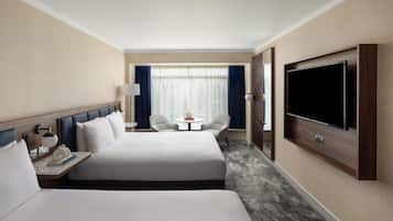 A hotel room with two beds, a TV, a desk with a lamp, a small table, and a chair.
