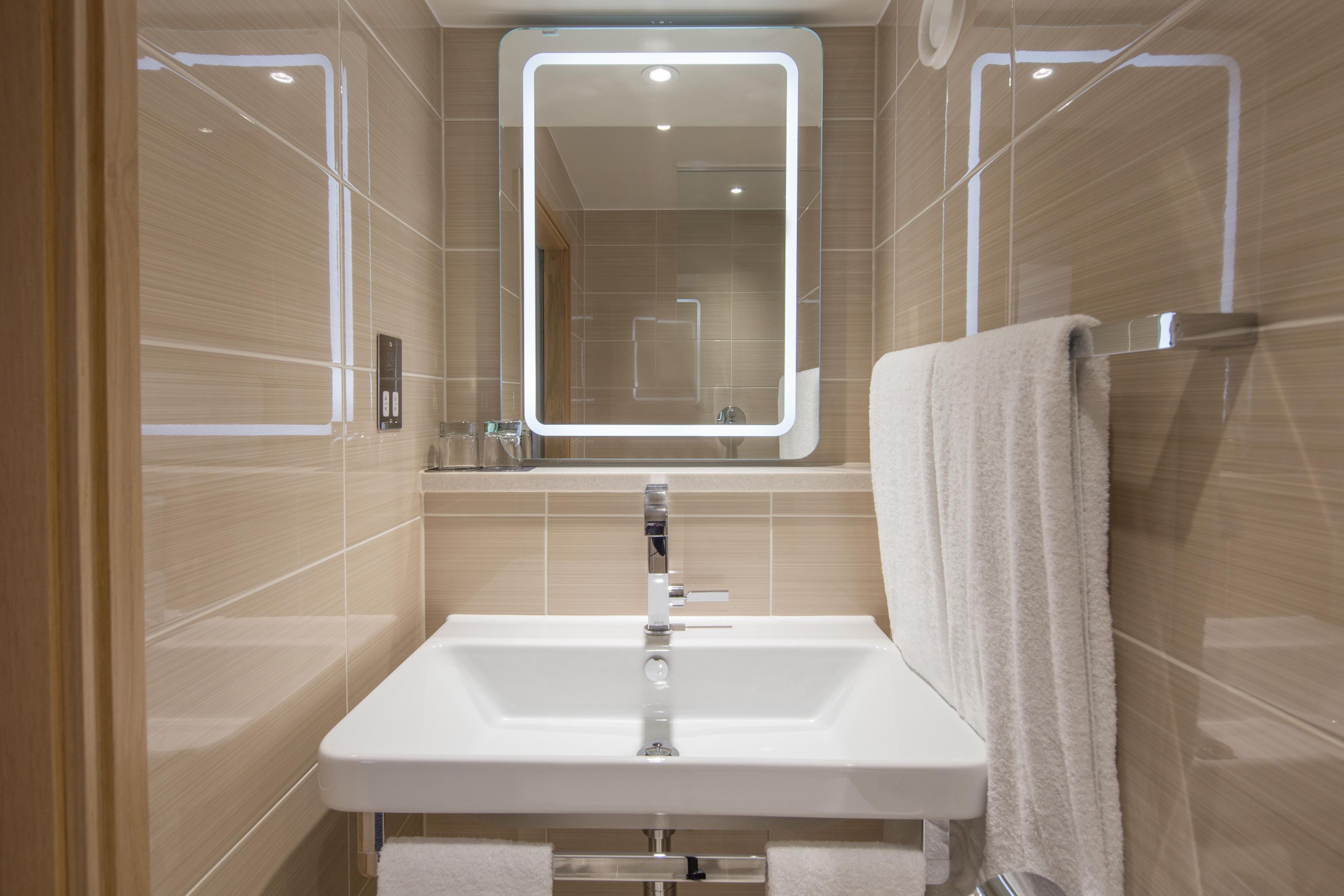 A modern bathroom with a white sink, a mirror, and a towel rack.