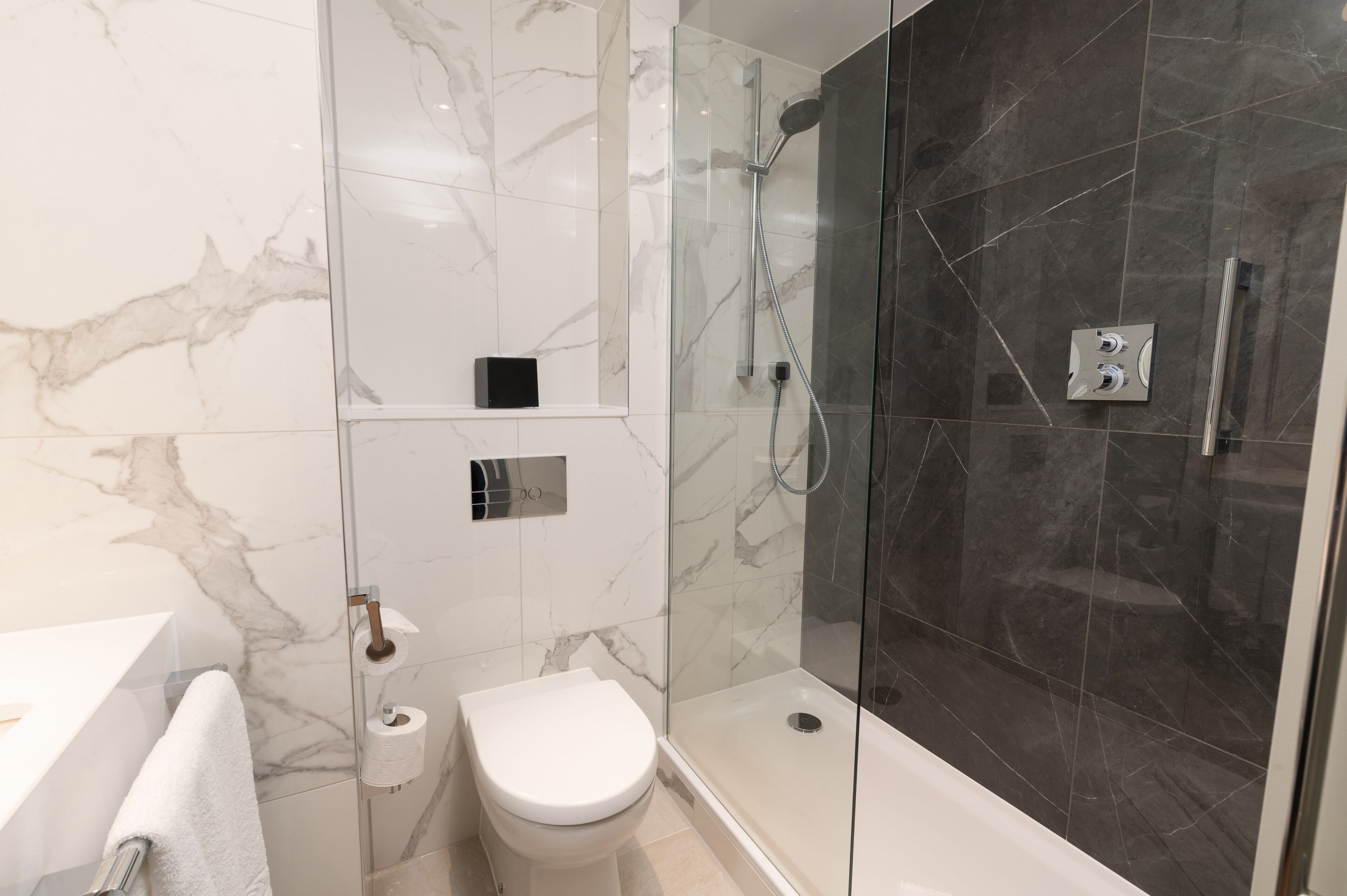 Une salle de bain moderne avec une douche à parois de verre, des toilettes et un mur recouvert de carreaux de marbre.