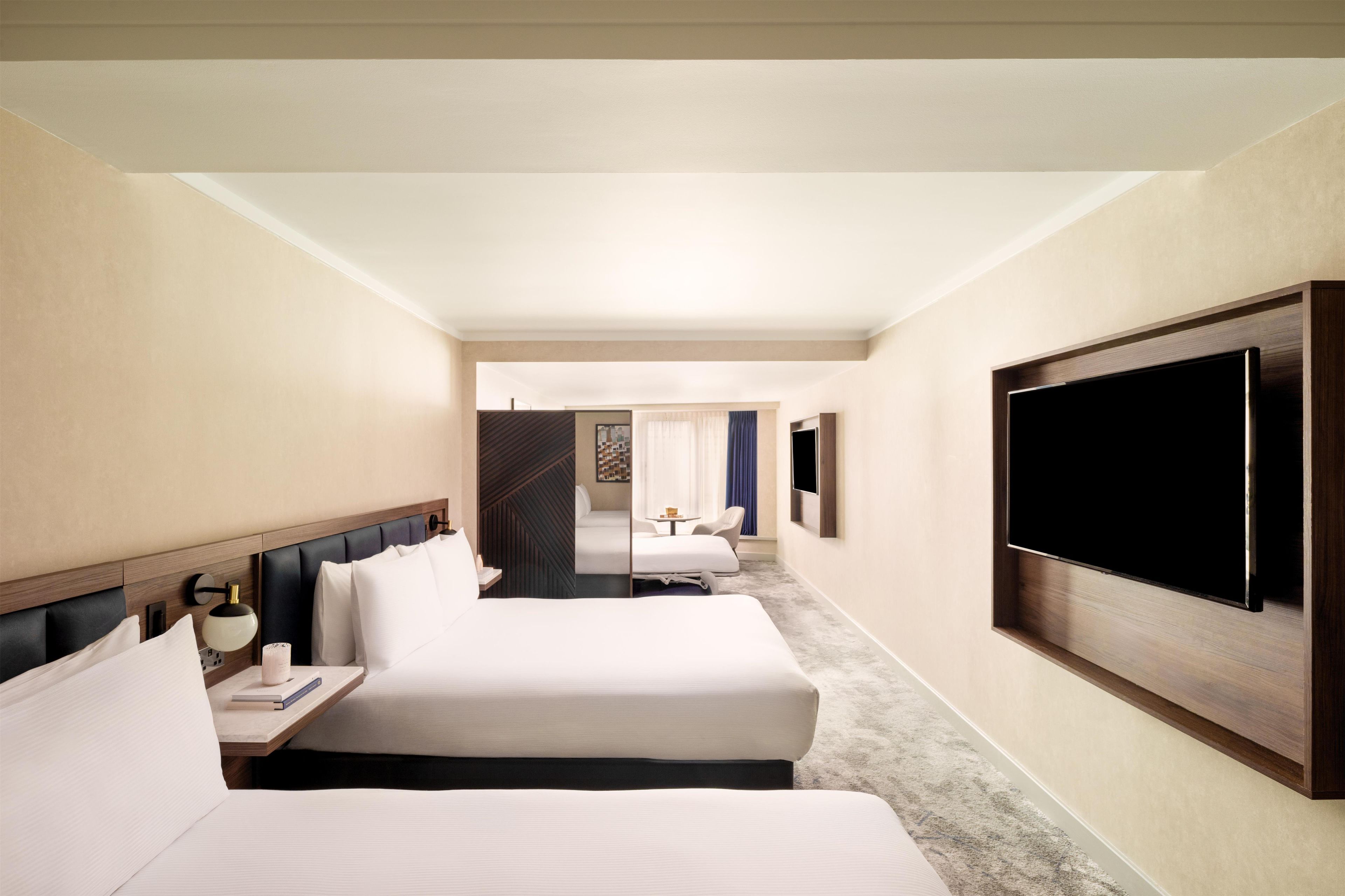 Habitación de hotel con dos camas, televisor y escritorio con lámpara.