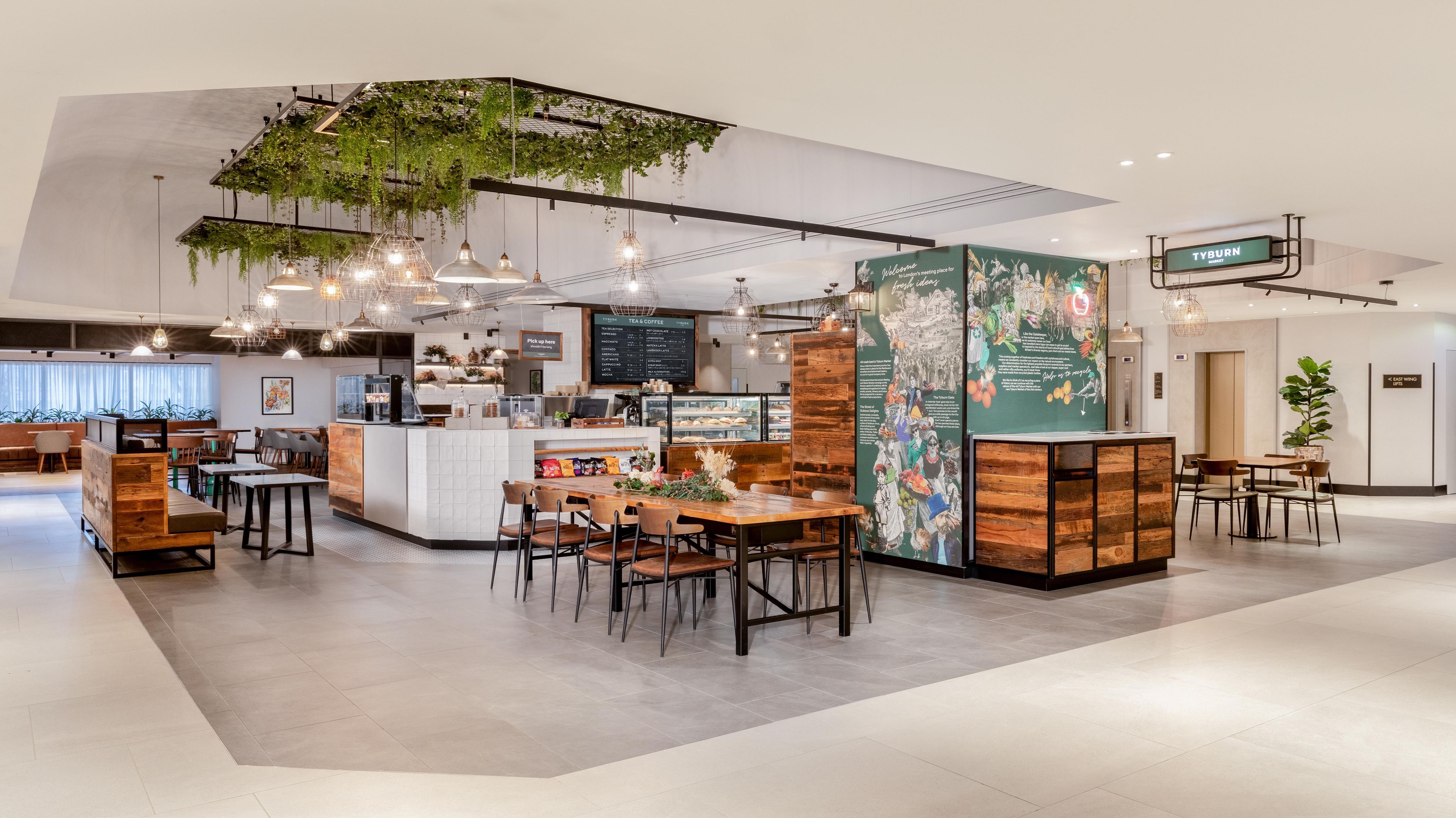 A modern cafe with a central counter, seating area, and decorative plants.