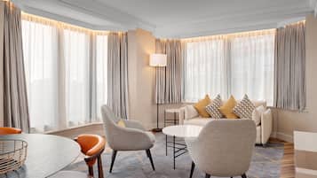 Una habitación de hotel moderna con una mesa redonda, dos sillones, un sofá con cojines estampados y una lámpara de pie.