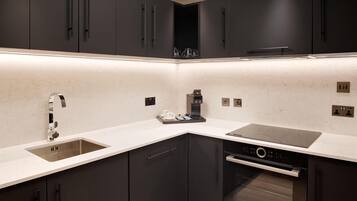 A modern kitchen with dark cabinets, a stainless steel sink, a built-in oven, and a coffee machine.
